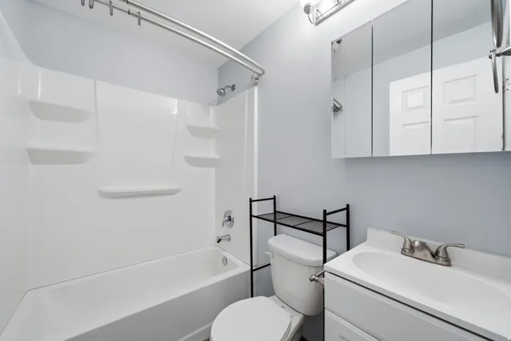 Contemporary full bathroom featuring a white subway tile surround with integrated shelving, a white vanity with brushed nickel faucet and mirrored medicine cabinet, a toilet with decorative metal towel rack, and a bathtub-shower combination with chrome fi