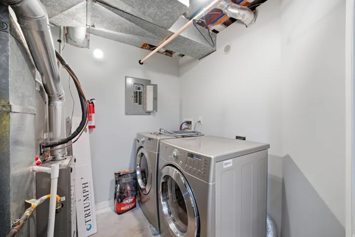 Utility space featuring a furnace, exposed ductwork, circuit breaker panel, and overhead lighting