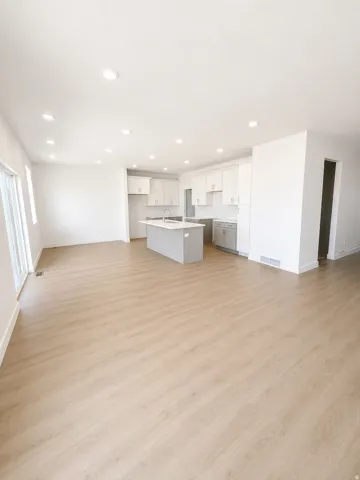 Open-concept living area featuring wood-finish flooring, recessed lighting, white walls, and a kitchen with an island and light cabinetry