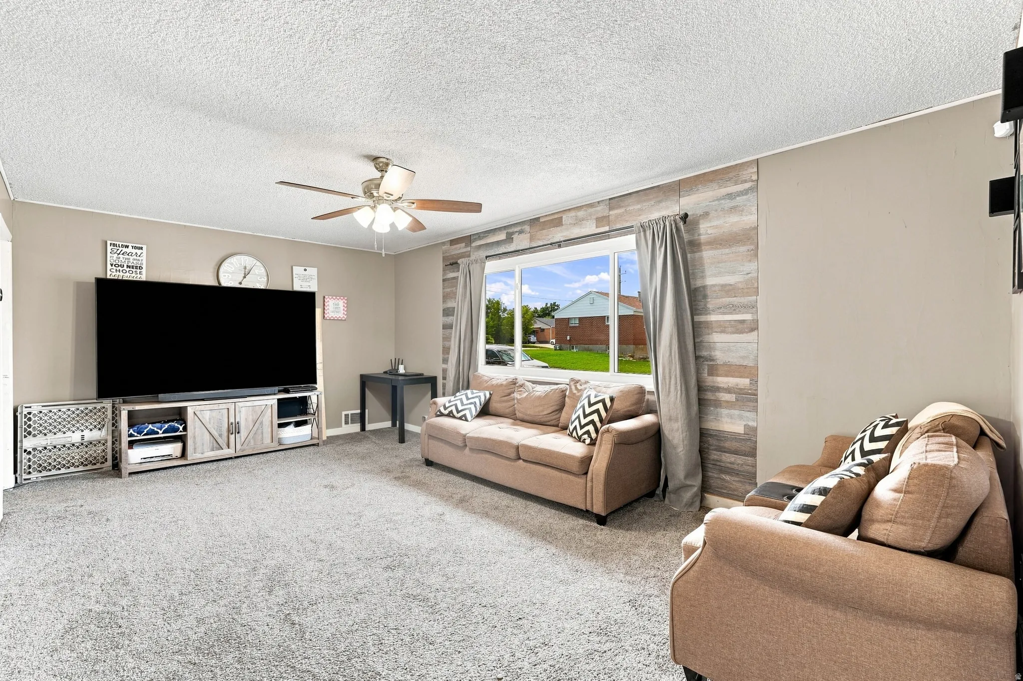 Expansive carpeted living space featuring a ceiling fan, a large window, and a decorative wood-finish accent wall