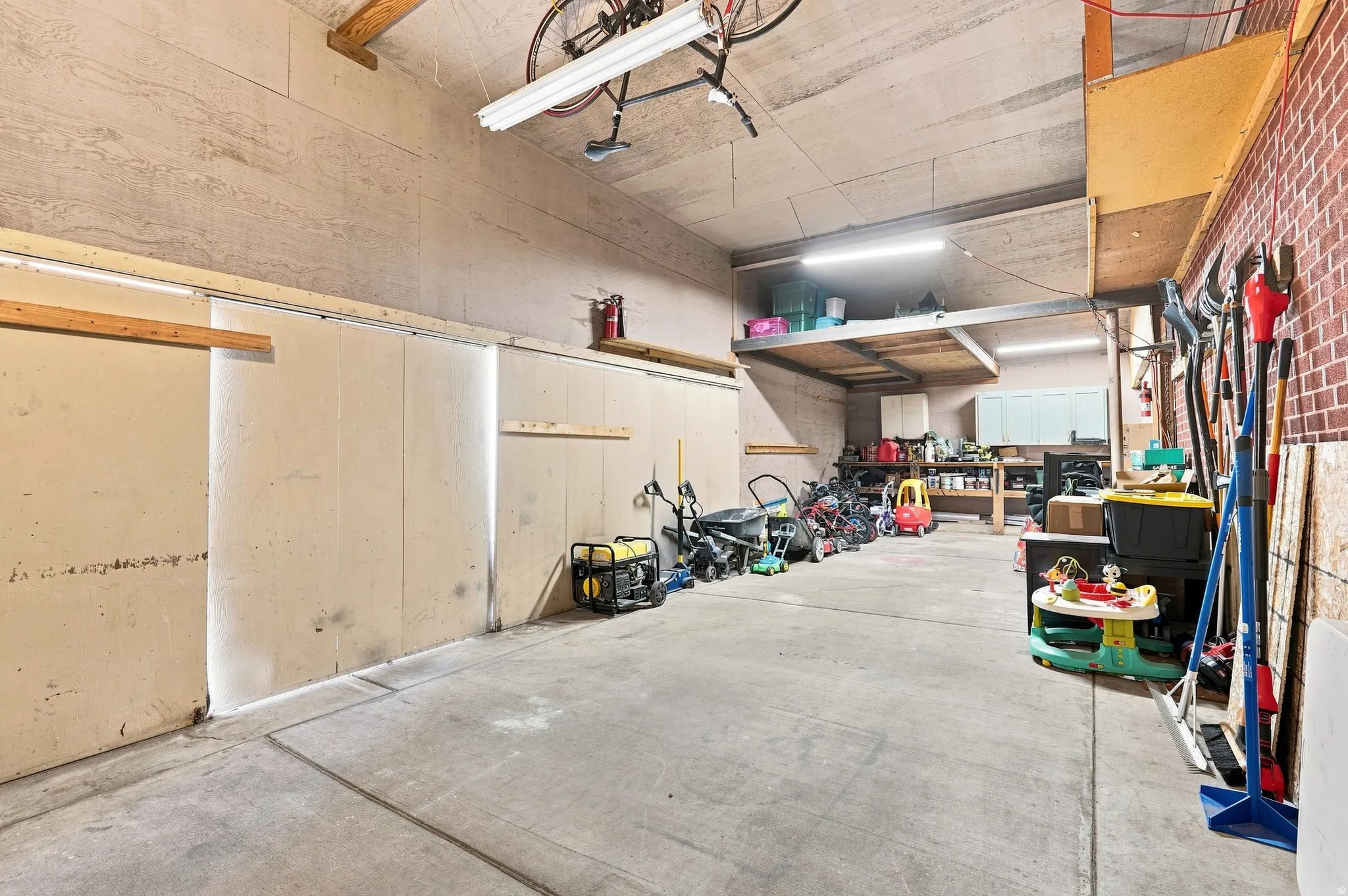 Concrete flooring with an exposed beam ceiling, brick accent wall, and built-in storage shelving
