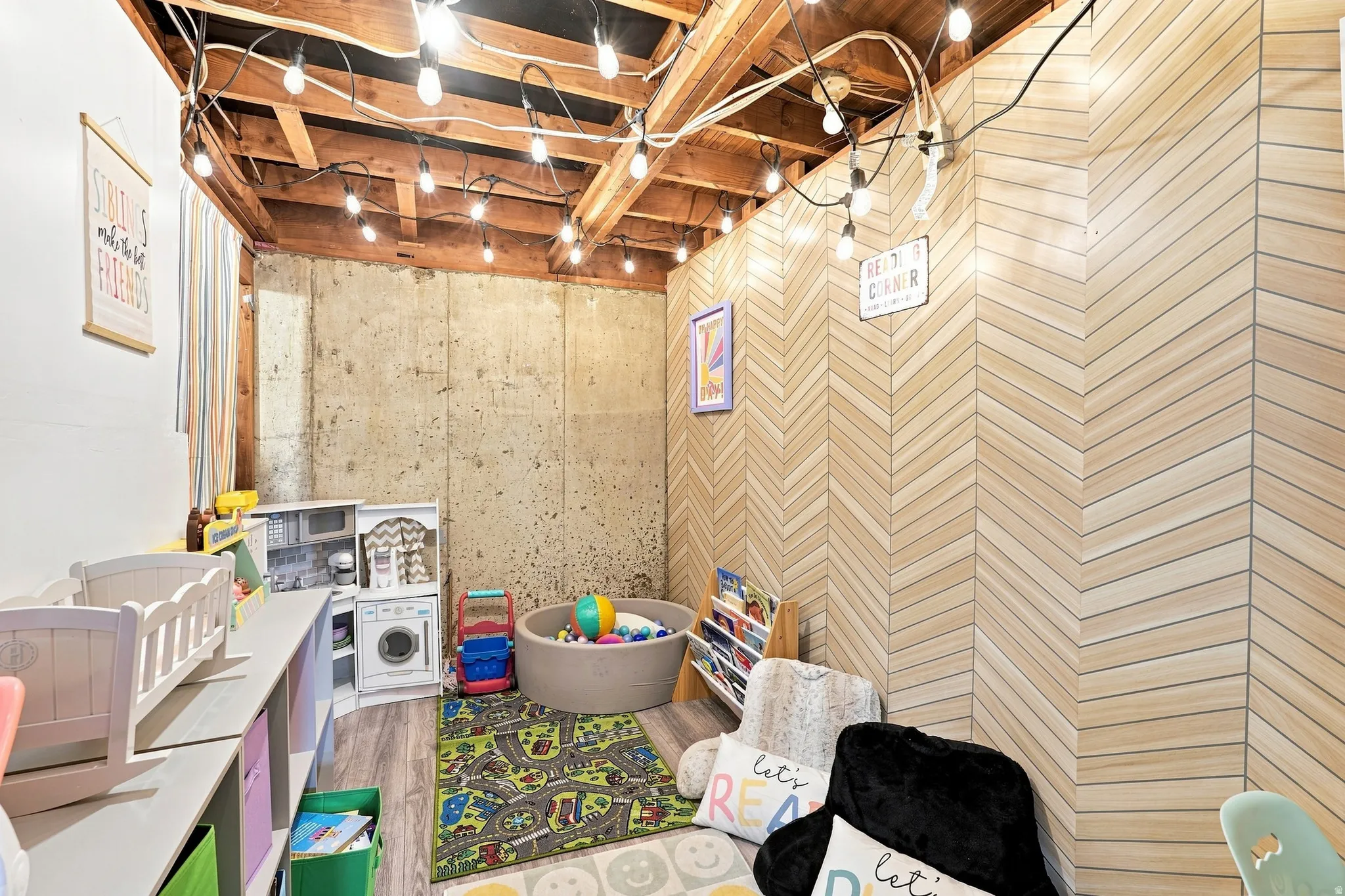 Exposed ceiling beams, string lighting, wood-finish chevron accent wall, concrete foundation wall, and wood-finish flooring