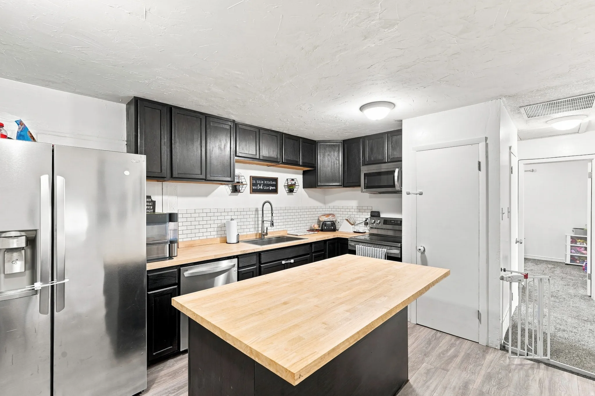 Kitchen featuring dark cabinetry, wood-finish countertops, stainless steel appliances, a subway tile backsplash, and an island with a wood-finish top