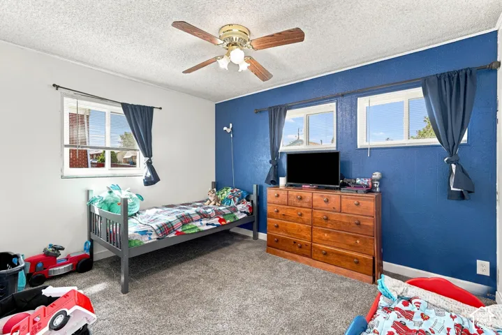 Room featuring neutral-toned carpeting, a textured ceiling, a ceiling fan with light fixture, and dual-pane sliding windows