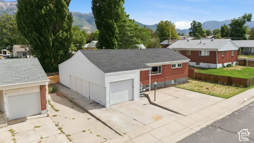Ranch-style exterior featuring brick and horizontal siding, a multi-car garage, expansive concrete driveway, and mountain backdrop