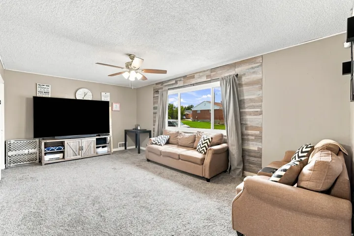 Expansive carpeted living space featuring a ceiling fan, a large window, and a decorative wood-finish accent wall