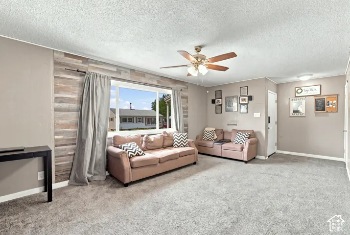 Living area featuring textured ceiling, large picture window, wood-paneled accent wall, and ceiling fan with multi-light fixture
