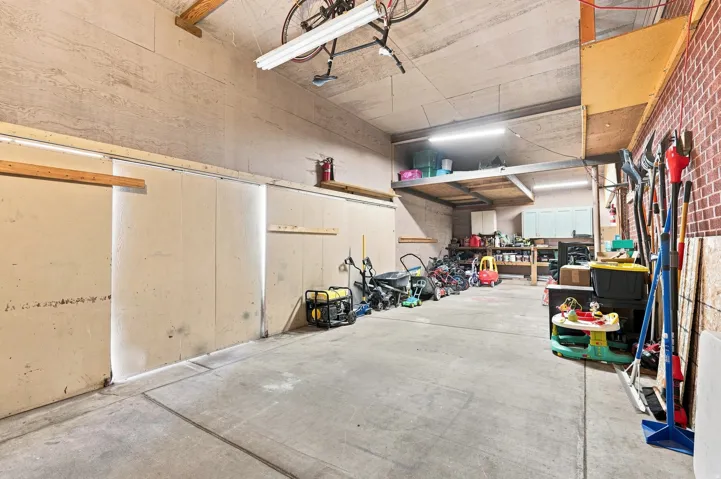Concrete flooring with an exposed beam ceiling, brick accent wall, and built-in storage shelving