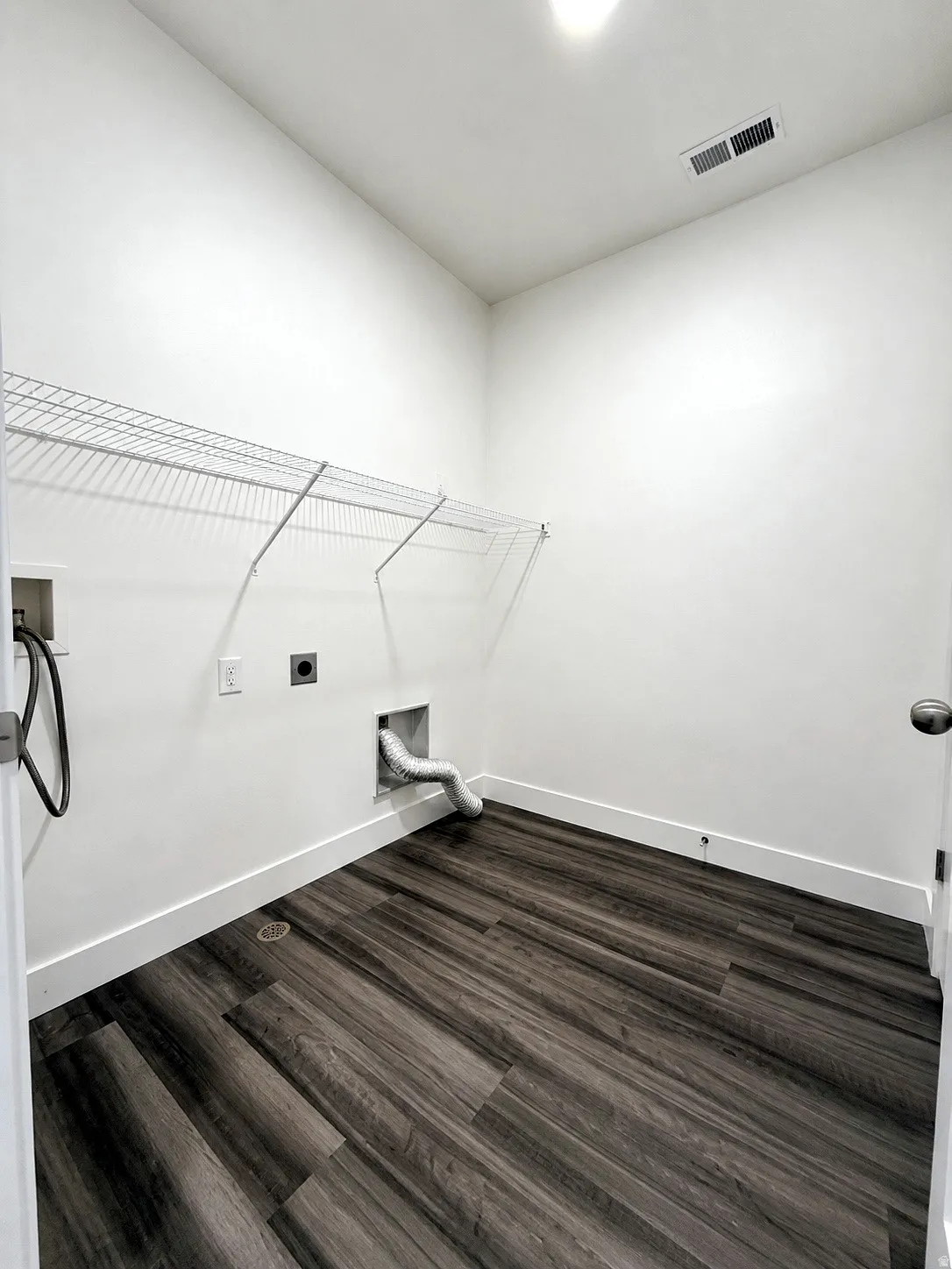Laundry area featuring wood-finish flooring, white walls, and a built-in wire shelf