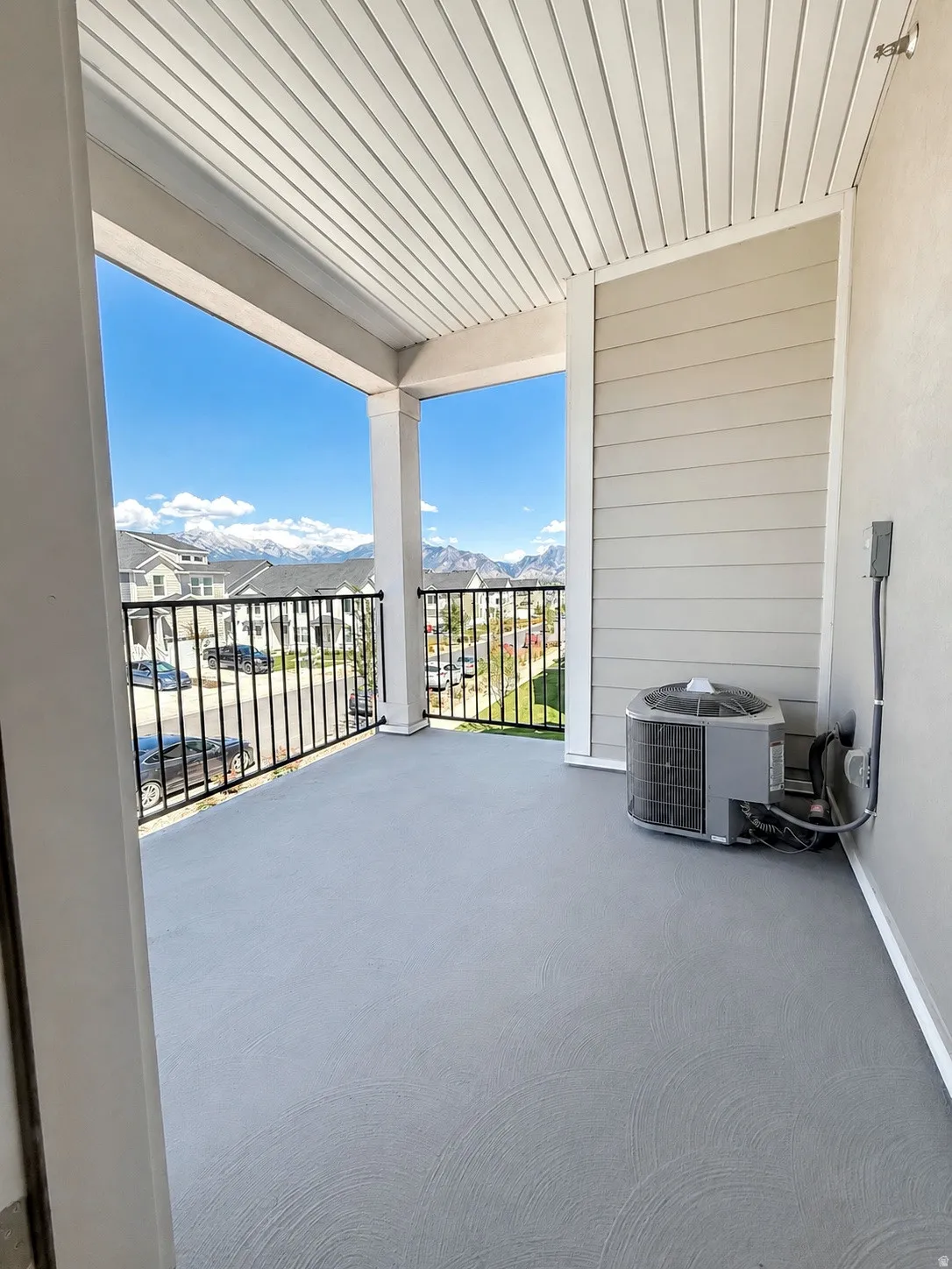 Covered outdoor patio with a textured gray surface, white soffit ceiling, and black metal railing