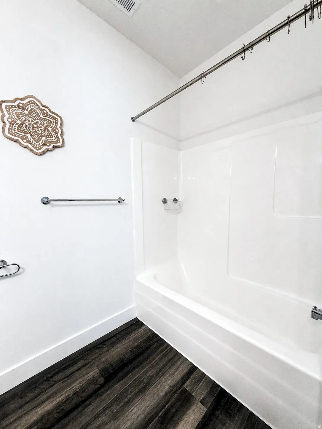 White acrylic tub and shower combination with chrome fixtures, complemented by dark wood-finish flooring