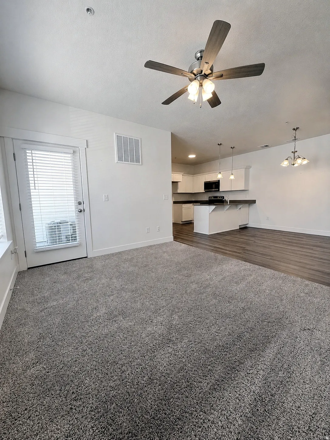 Wall-to-wall carpeting, overhead ceiling fan with light fixture, white interior walls, white kitchen cabinetry with black appliances, and dark wood-finish flooring
