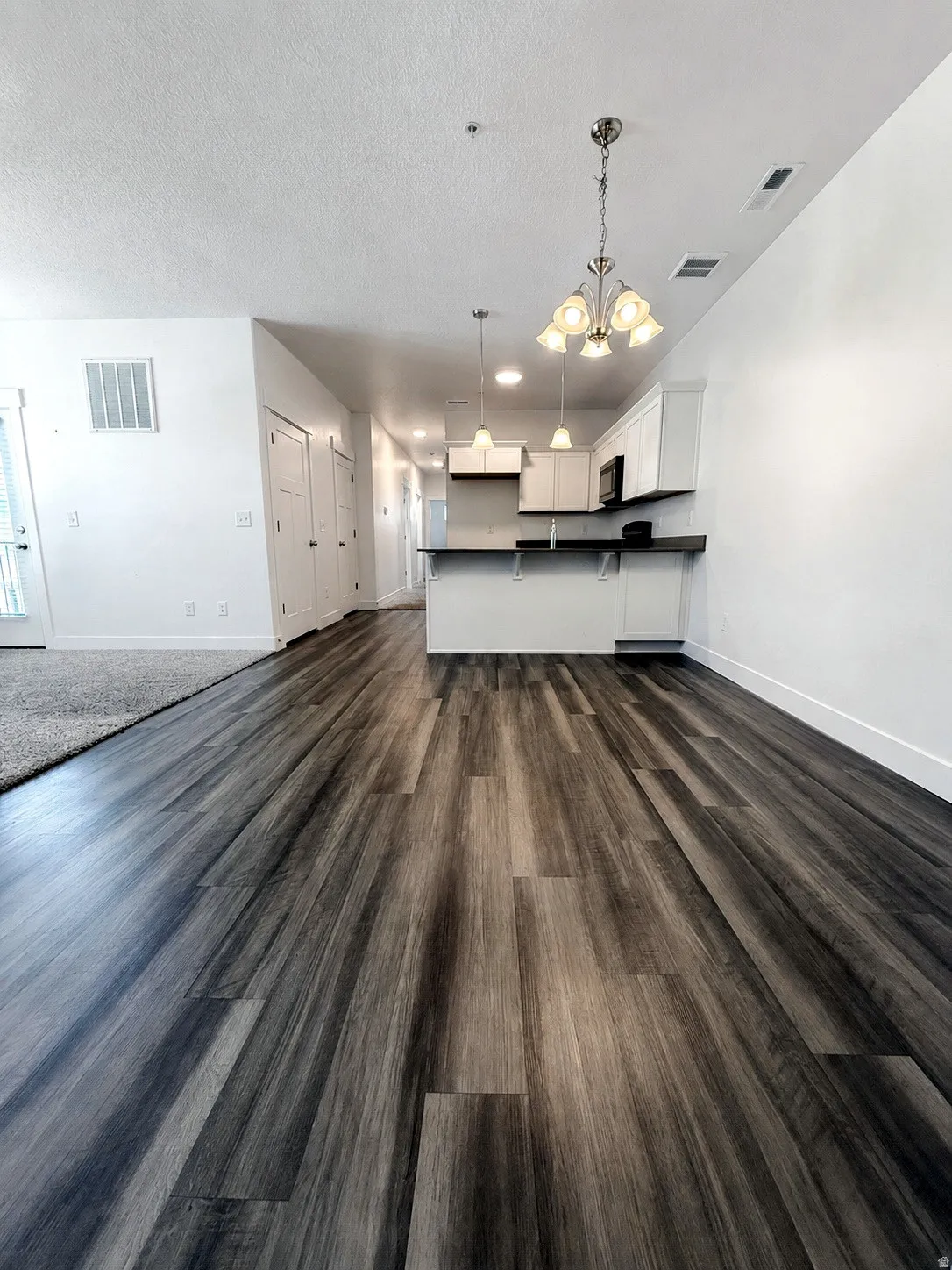 Wood-finish flooring throughout, white walls, kitchen with white cabinetry, dark countertops, and pendant lighting