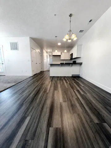 Wood-finish flooring throughout, white walls, kitchen with white cabinetry, dark countertops, and pendant lighting