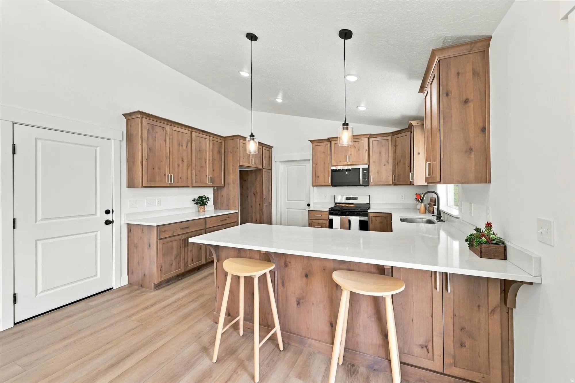 Vaulted ceiling kitchen featuring wood-finish cabinetry, white countertops, a subway tile backsplash, and wood-finish flooring