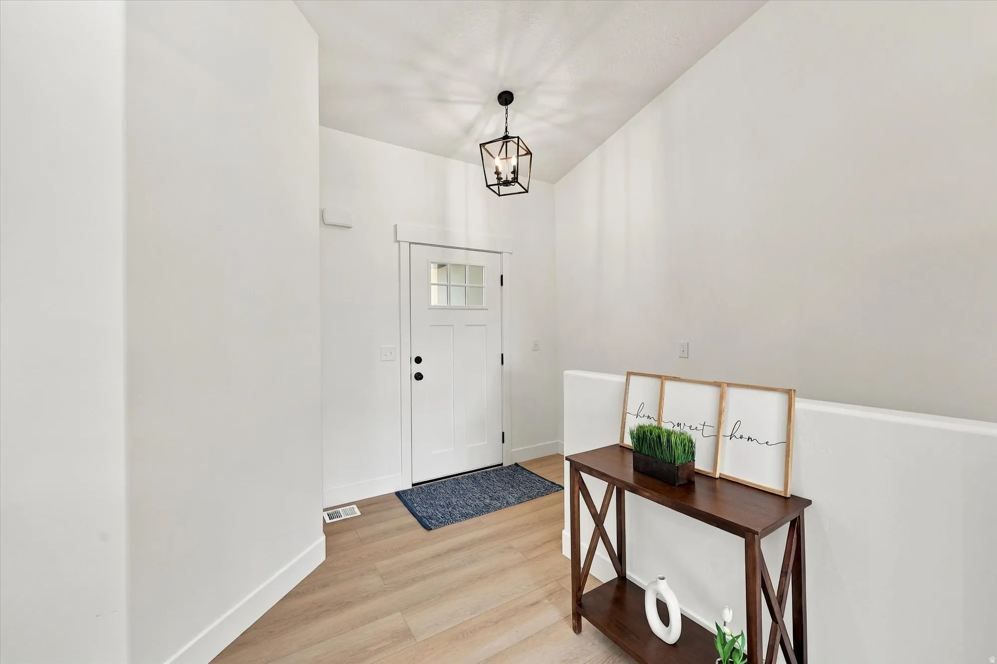 White entry door with upper glass panels, light wood-finish flooring, and a contemporary black metal light fixture