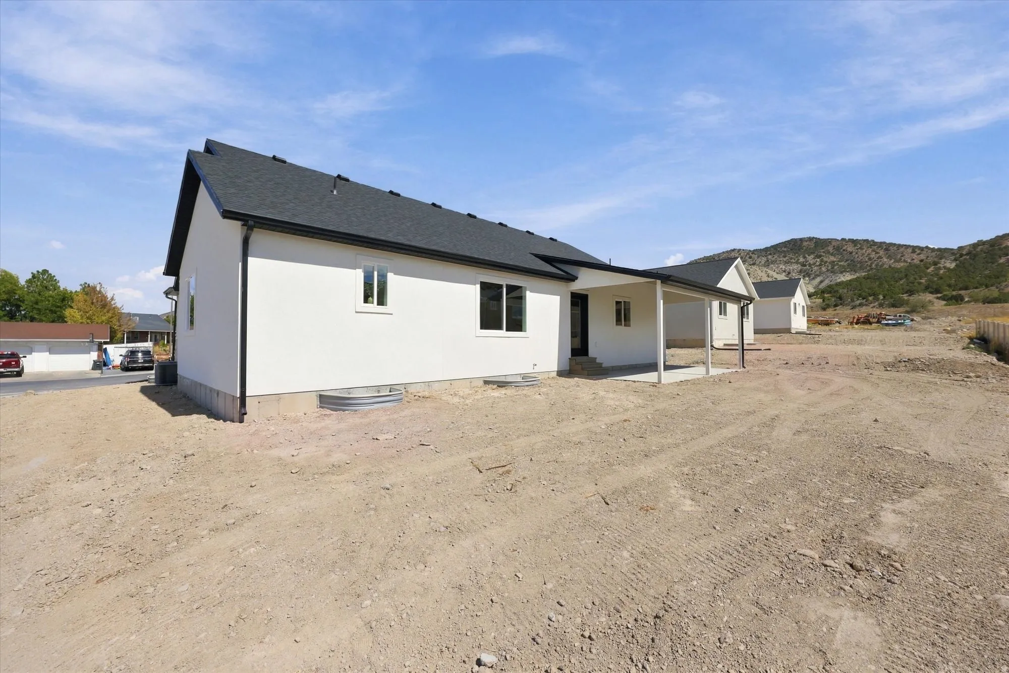 White stucco exterior with a covered patio, dark shingle roof, and distant mountain backdrop