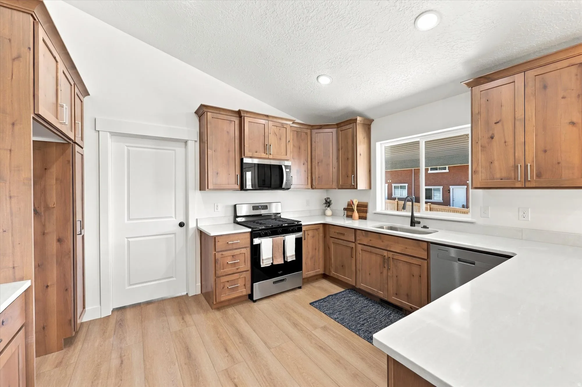 Kitchen featuring wood-finish cabinetry, stainless steel appliances, light-toned countertops, a stainless steel sink, and wood-finish flooring