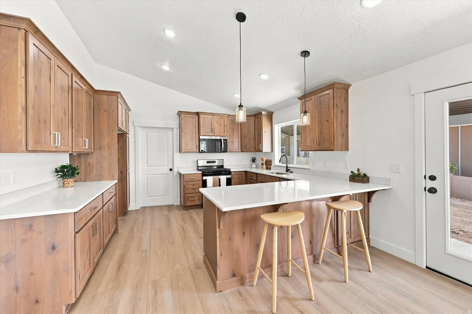 Vaulted ceilings, wood-finish flooring, wood cabinetry, built-in microwave, and pendant lighting
