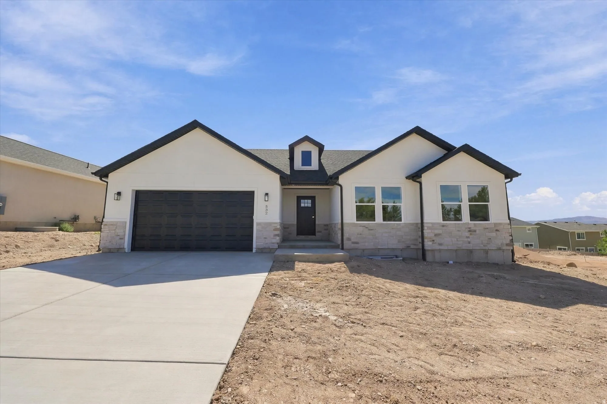 White stucco exterior with stone accents, black roof, and dark garage door
