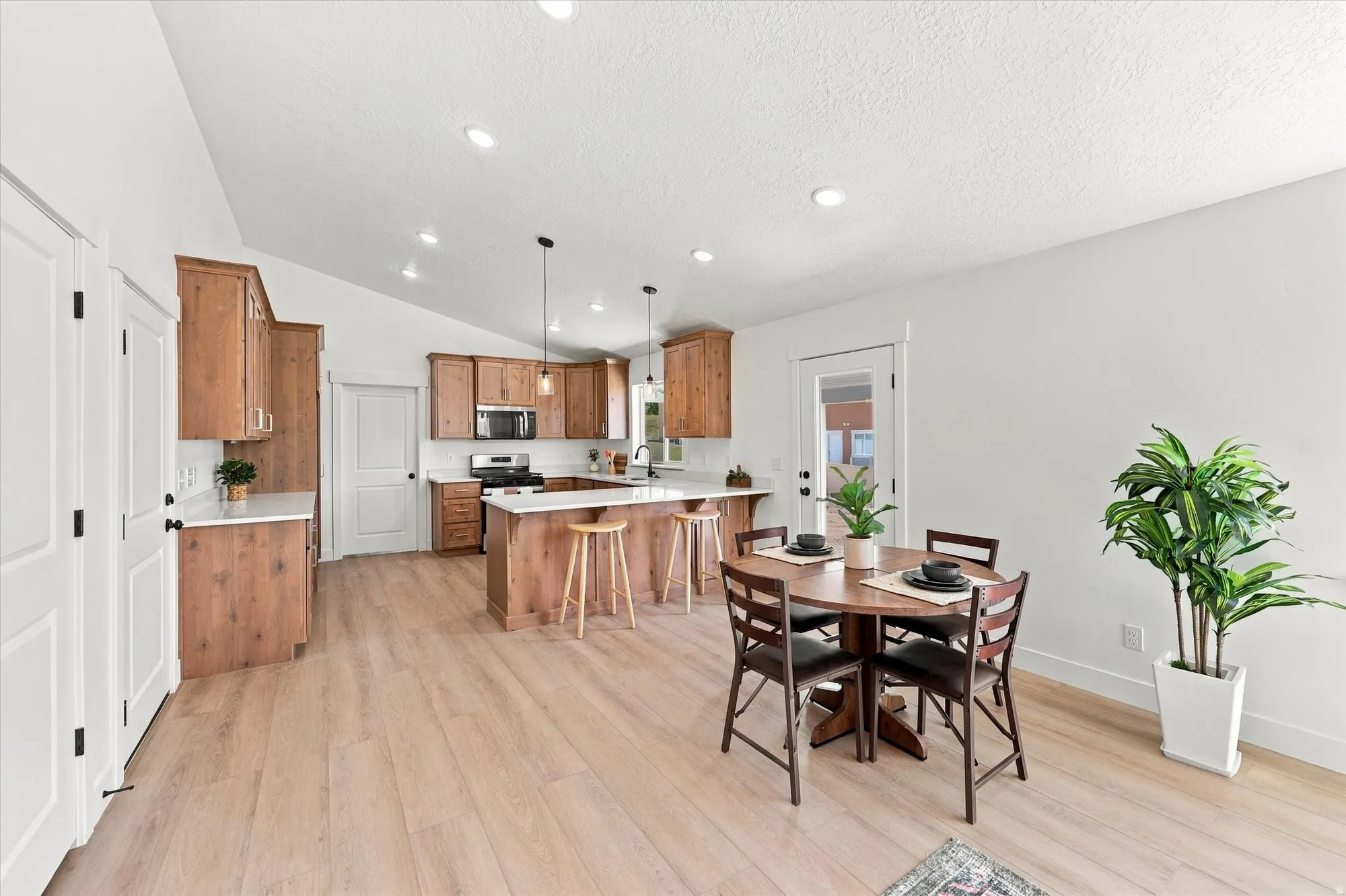 Open-concept living area with vaulted ceilings, wood-finish flooring, natural wood cabinetry, and a kitchen island with seating