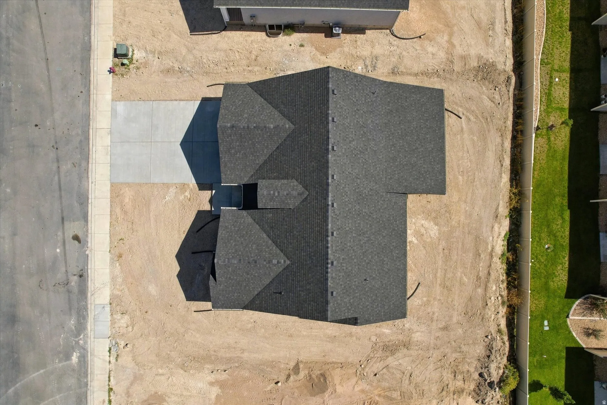 Gabled roofline with dark shingles, concrete driveway, and a partially developed surrounding lot