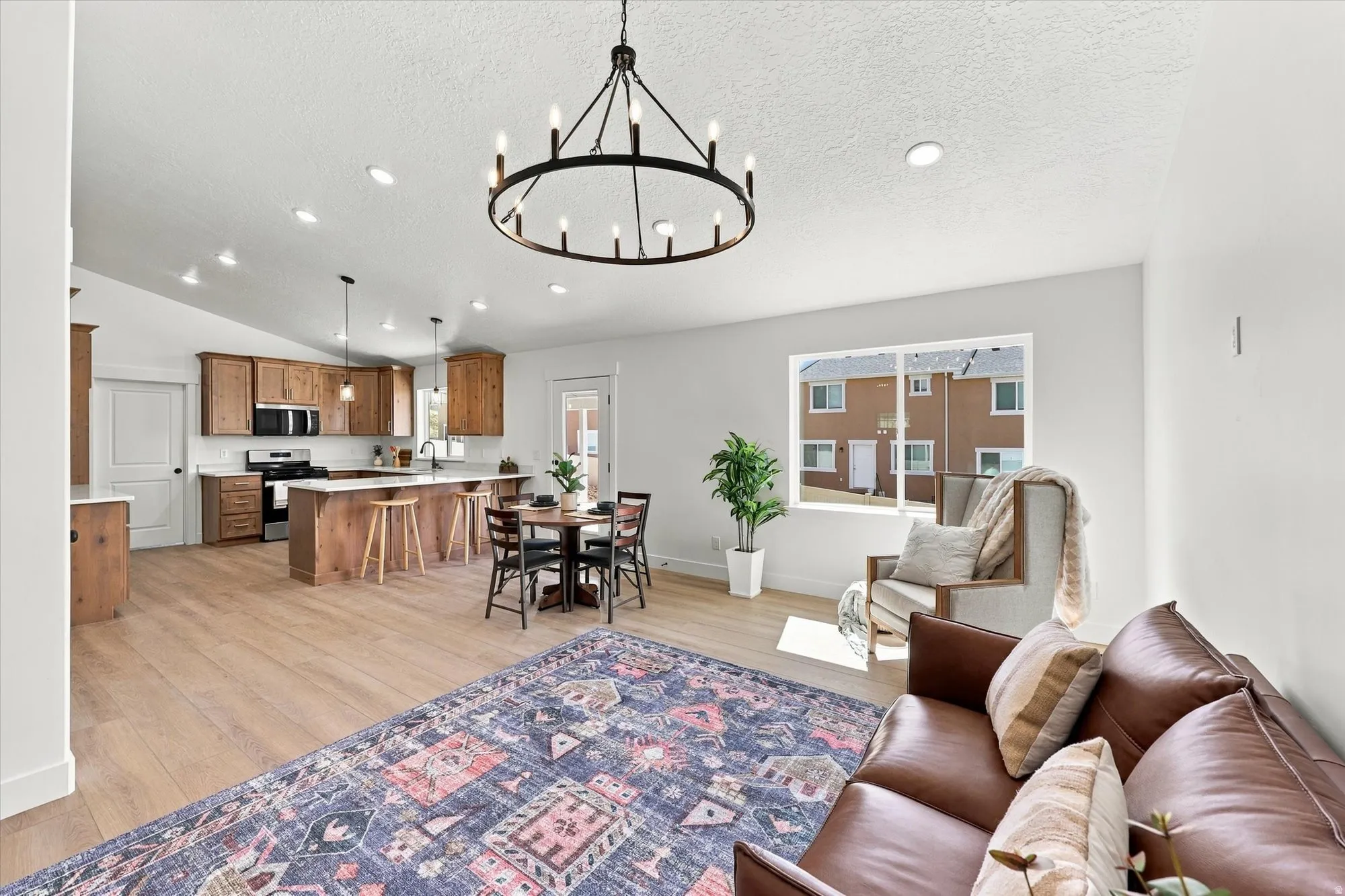 Open-concept living area with wood-finish flooring, vaulted ceilings, recessed lighting, and a modern chandelier