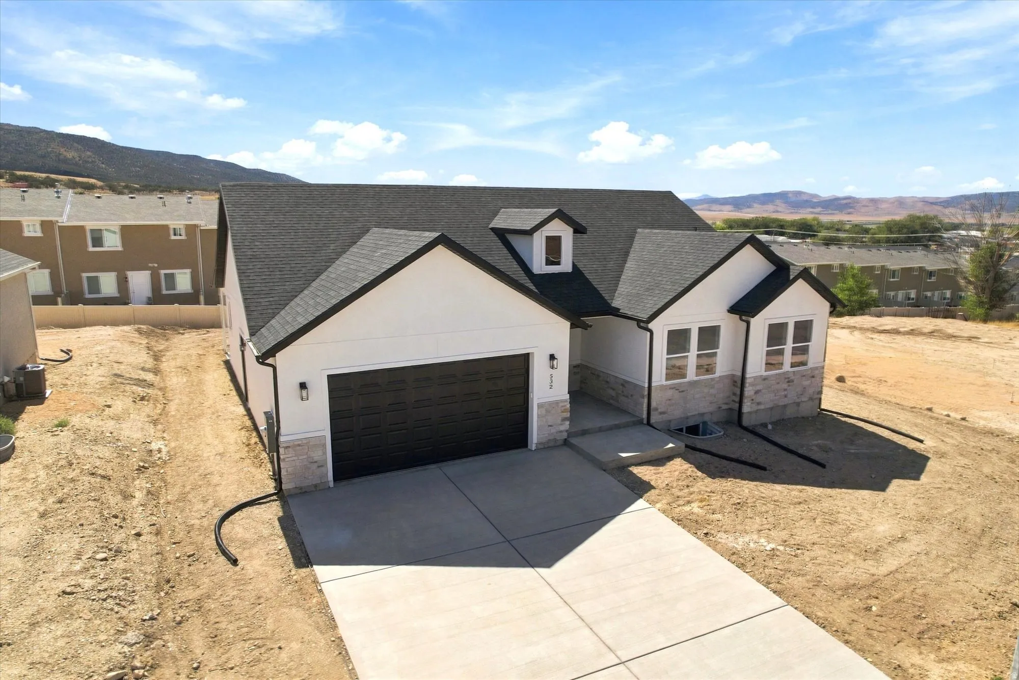 Contemporary exterior featuring white siding, stone veneer accents, dark trim, a two-car garage, and a concrete driveway