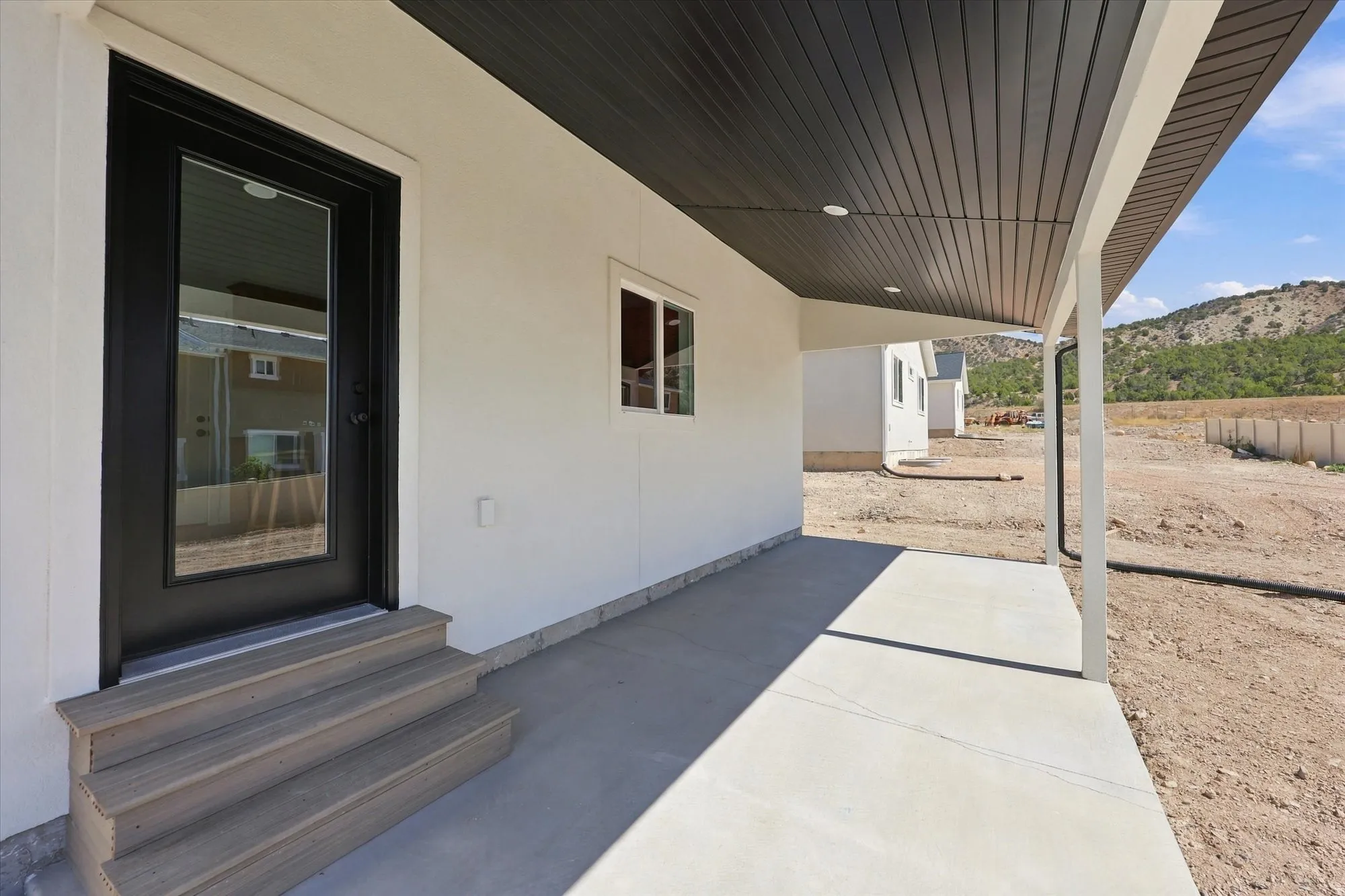 Covered porch with concrete flooring, black full-light entry door, and wood-finish steps