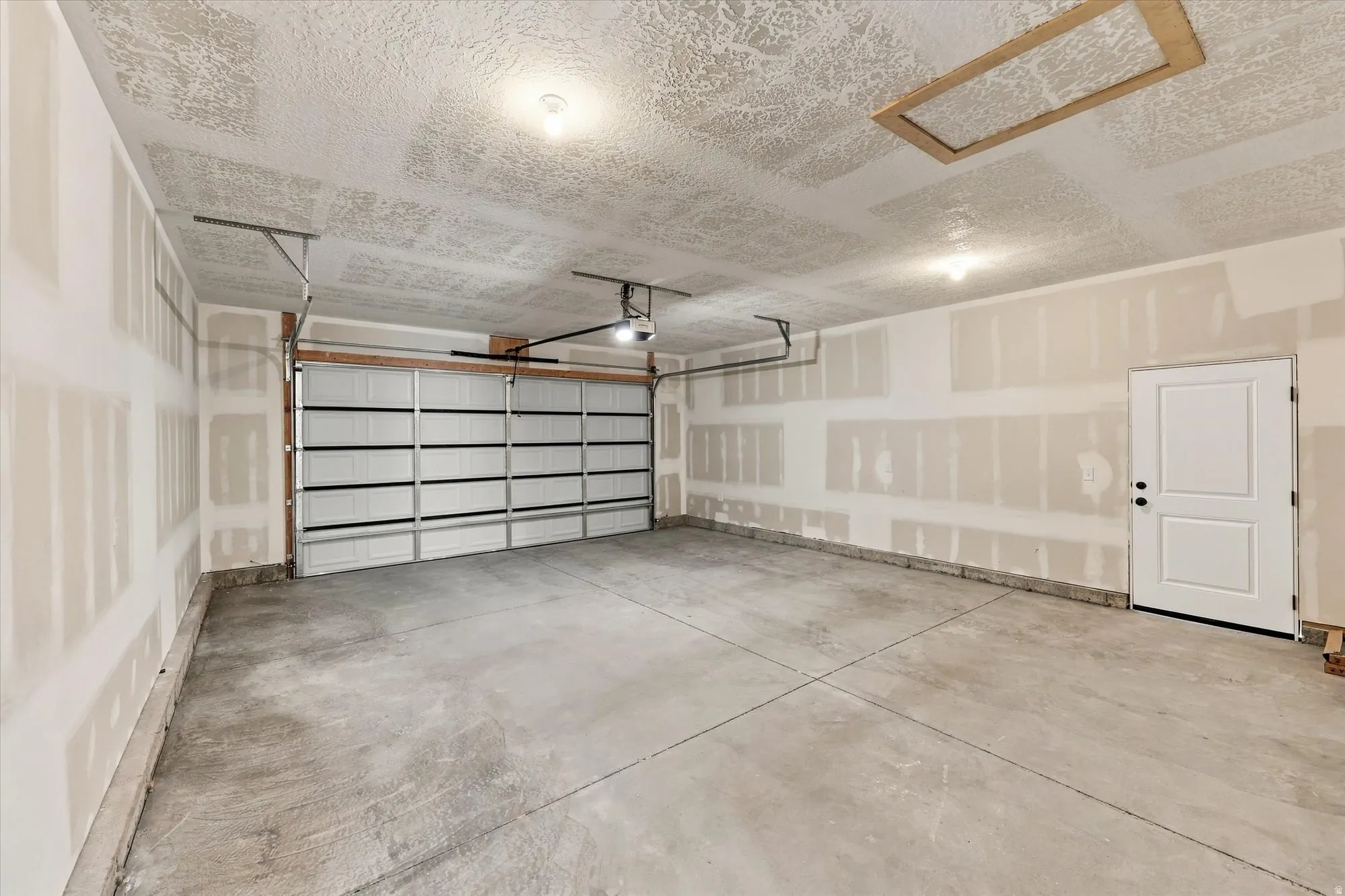 Spacious garage with concrete flooring, automatic overhead door, overhead lighting, and a paneled entry door