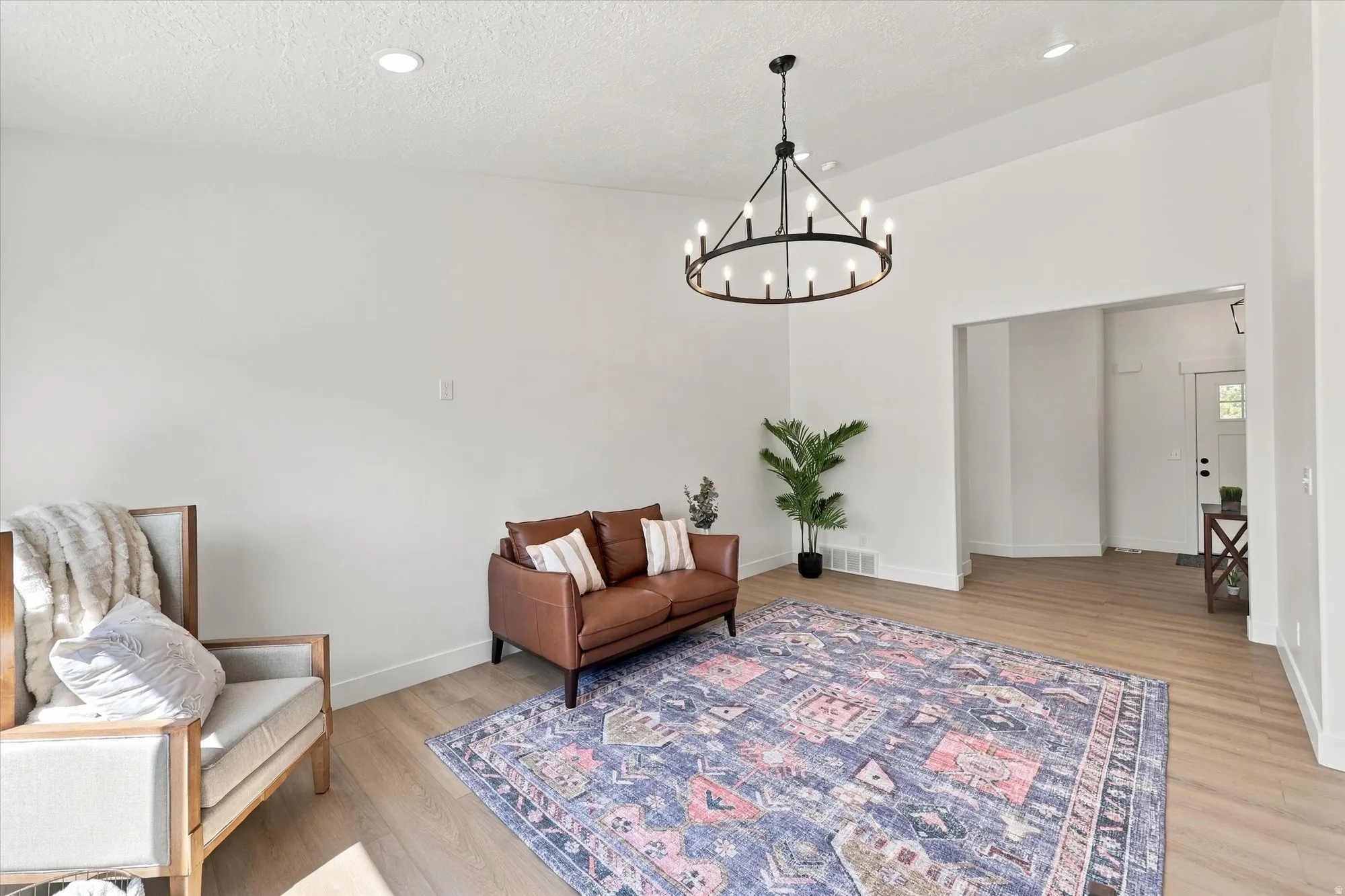 Open-concept living space with high ceilings, recessed lighting, wood-finish flooring, and a contemporary chandelier