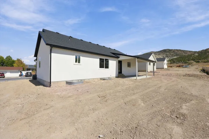 White stucco exterior with a covered patio, dark shingle roof, and distant mountain backdrop