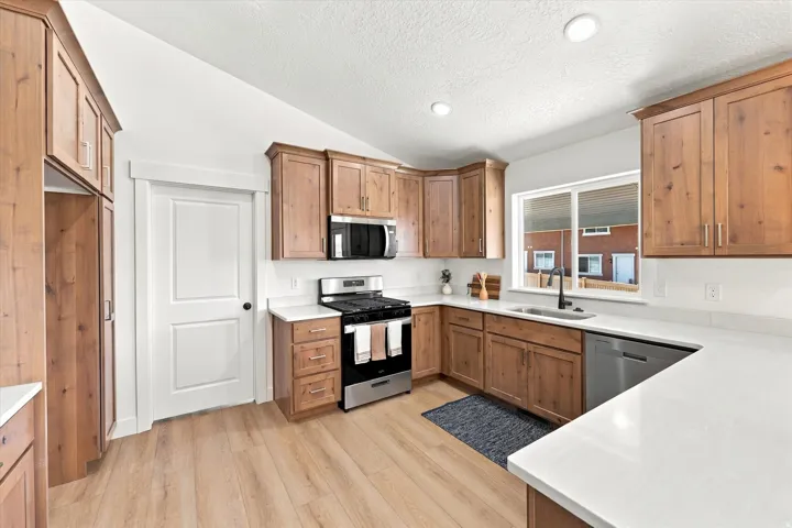 Kitchen featuring wood-finish cabinetry, stainless steel appliances, light-toned countertops, a stainless steel sink, and wood-finish flooring