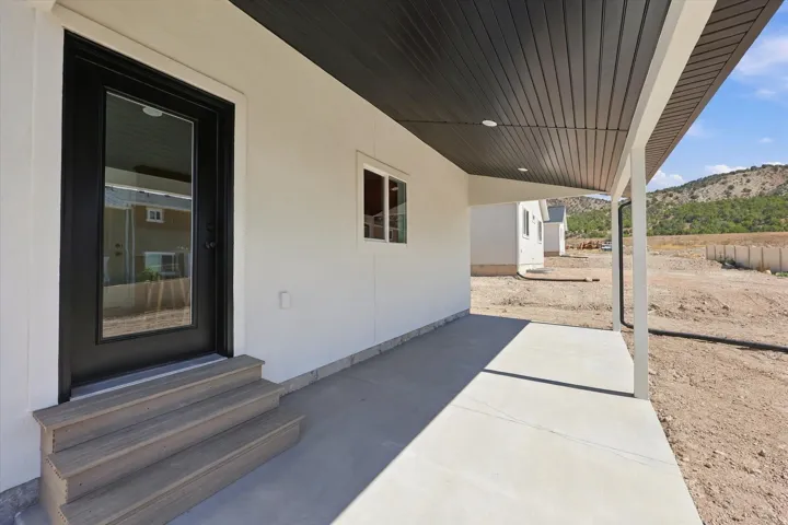 Covered porch with concrete flooring, black full-light entry door, and wood-finish steps