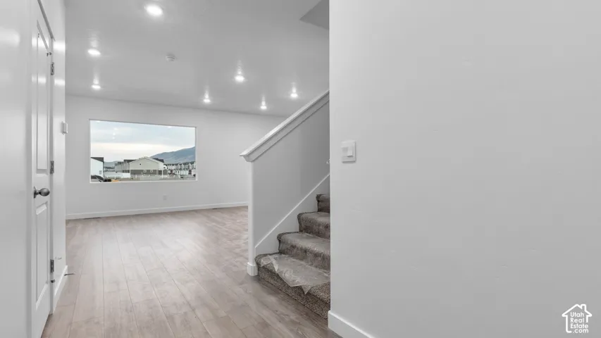 Recessed ceiling lighting, wood-finish flooring, broad window, and carpeted stairs with white railing