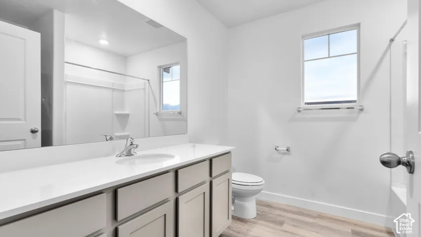 Bathroom featuring a single vanity with a white countertop, chrome faucet, a large mirror, and wood-finish flooring