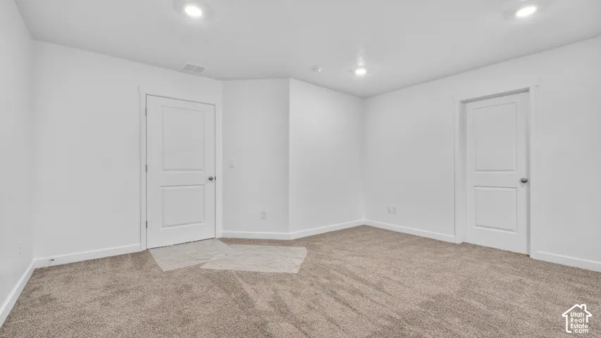 Recessed lighting illuminates the space, featuring white walls and neutral-toned carpeting