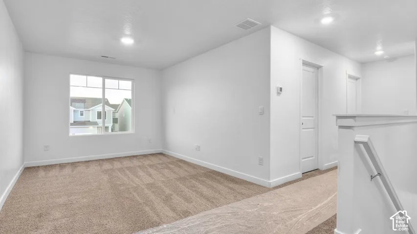 Spacious room with plush carpeting, natural light from a large window, recessed lighting, and crisp white walls