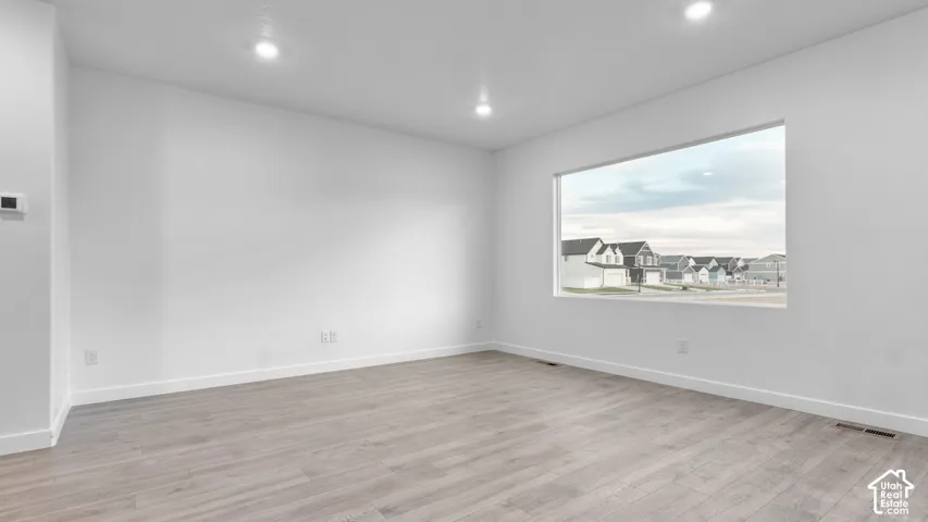 Recessed ceiling lighting, wide plank wood-finish flooring, white wall paint, and a rectangular window