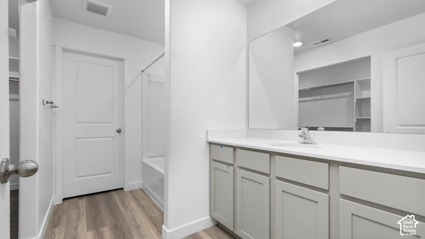 White vanity with an integrated sink and chrome faucet, wood-finish flooring, and a white shower/tub combination