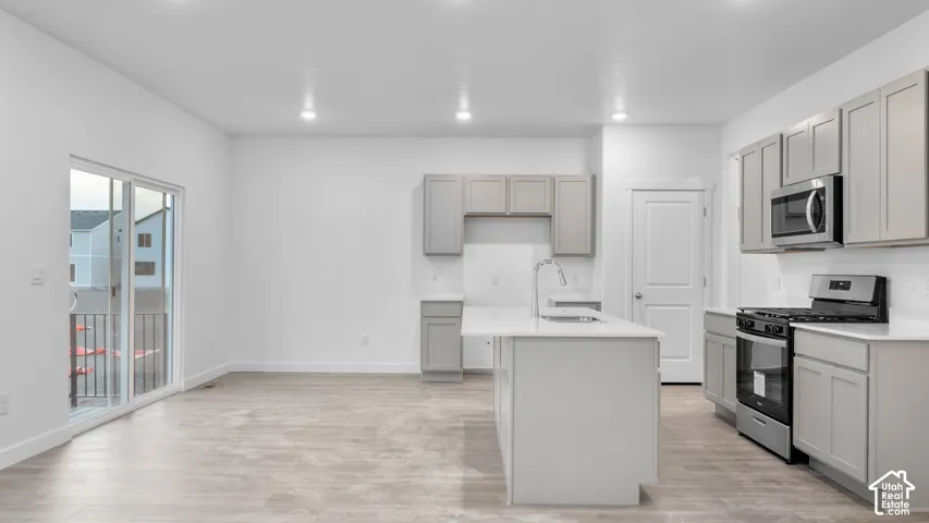 Kitchen featuring stainless steel appliances, light gray cabinetry, a central island with an undermount sink, and recessed lighting