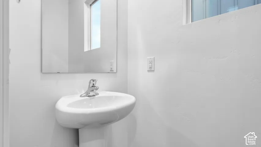 Pedestal sink with chrome faucet, framed mirror, and natural light from transom window