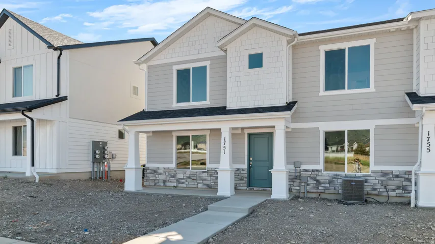 Contemporary facade featuring light-colored siding, decorative stone accents, a covered entry, and a teal front door