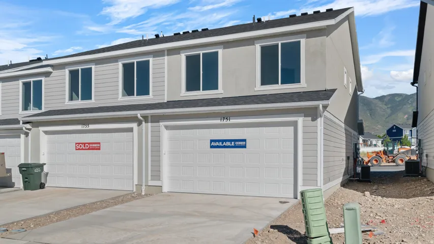 Two-story townhome with light gray siding and stucco exterior, dark shingle roof, white trim windows, and an attached garage with a concrete driveway