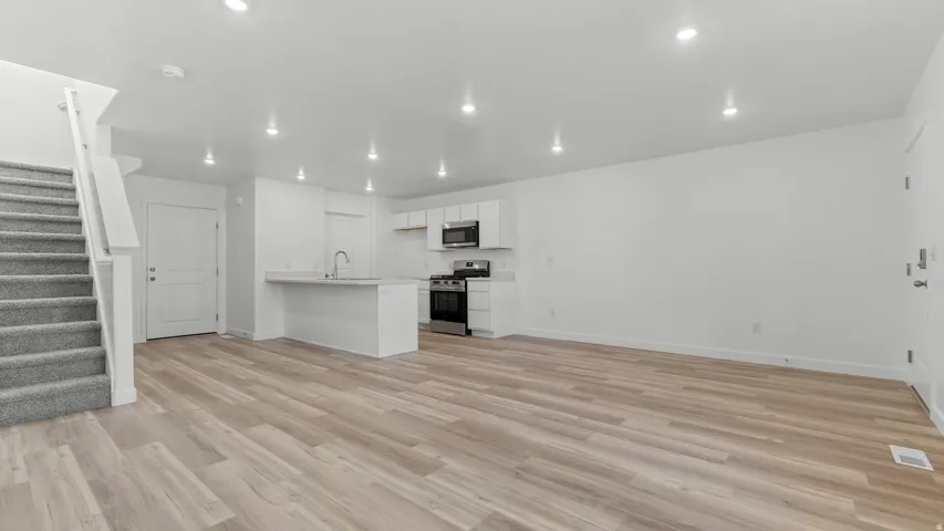 Open-concept living space featuring wood-finish flooring, recessed lighting, a white kitchen island with an undermount sink, white cabinetry, and stainless steel appliances