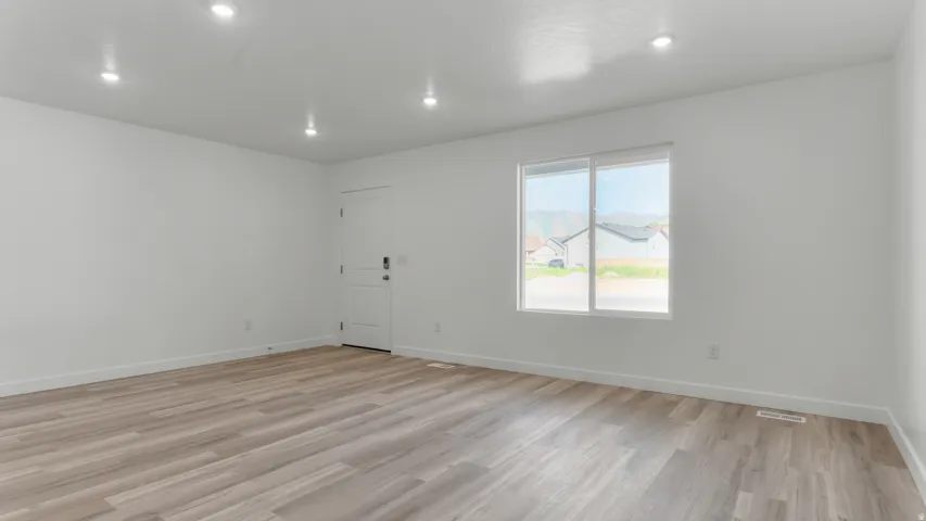 Spacious room featuring wood-finish flooring, recessed lighting, and a white paneled door