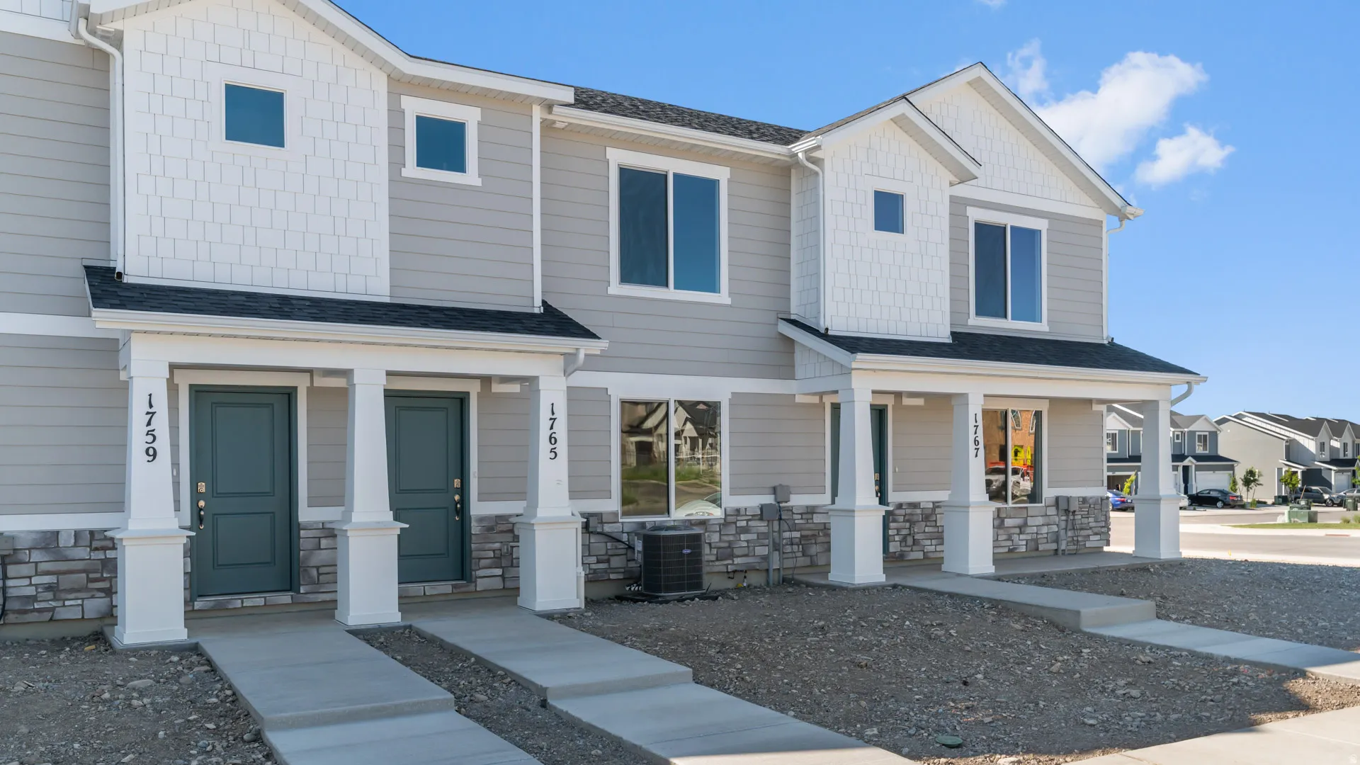 Modern townhome exterior featuring light gray siding, white trim, stone veneer accents, and a dark gray shingle roof