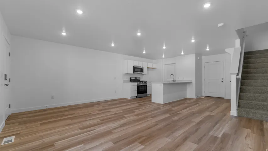Open-concept living space featuring wood-finish flooring, recessed lighting, and a kitchen with white cabinetry and stainless steel appliances