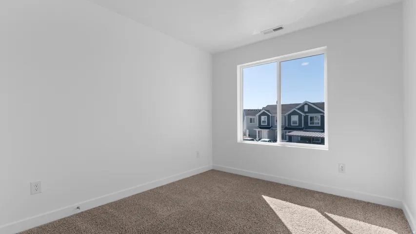 Bright room featuring a large window, neutral carpeting, and white walls