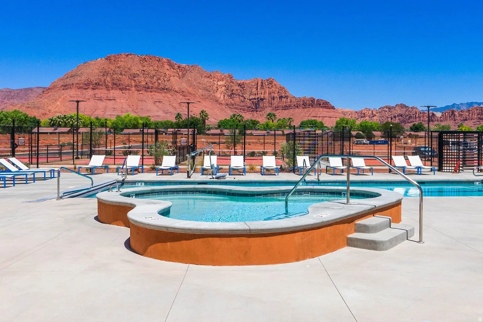 Swimming pool and spa with concrete surround, bordered by tennis courts and a distant mountain range